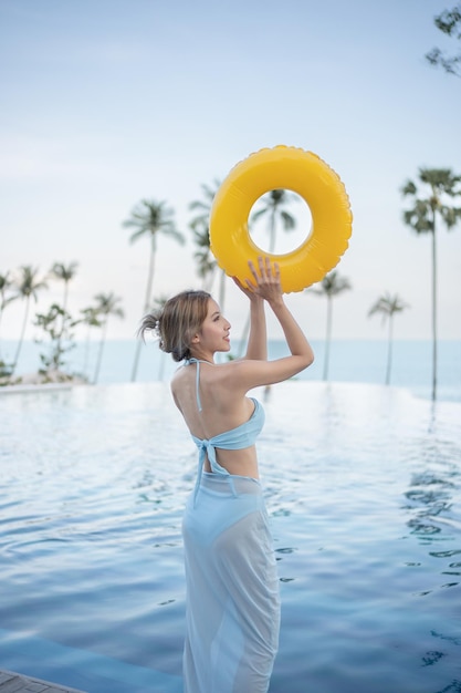 Vrouw draagt blauw zwempak poserend met gele opblaasbare rubberen ring