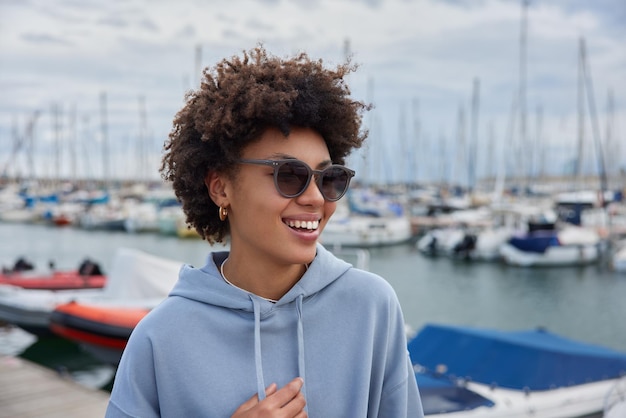 vrouw draagt casual hoodie wandelingen in de jachthaven in haar vrije tijd geniet van mooie uitzichten poseert in de haven tegen schepen en jachten brengt vakantie door in badplaats wandelingen langs de kust