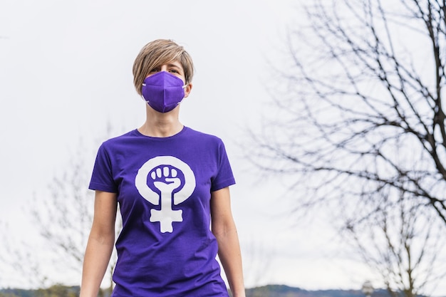 Vrouw draagt een paars T-shirt met het symbool van de werkende vrouw die vrouwenrechten claimt voor Internationale Vrouwendag op 8 maart en draagt een gezichtsmasker voor de coronaviruspandemie van 2020