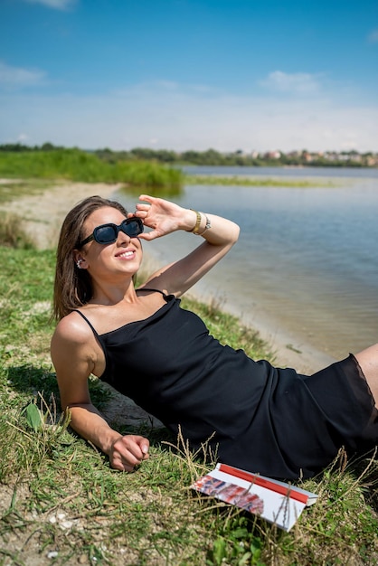 Vrouw draagt gestreepte zwarte jurk hoed en rode lippenstift liggend in de buurt van het meer in zomerdag