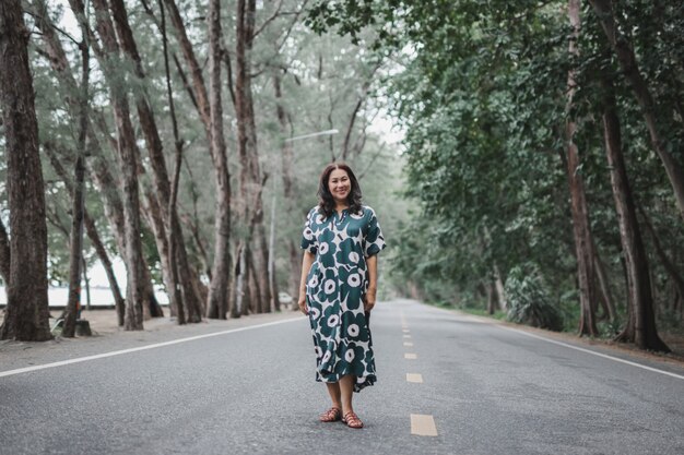 Vrouw draagt mooie lange jurk staande op de weg onder groene bomen.