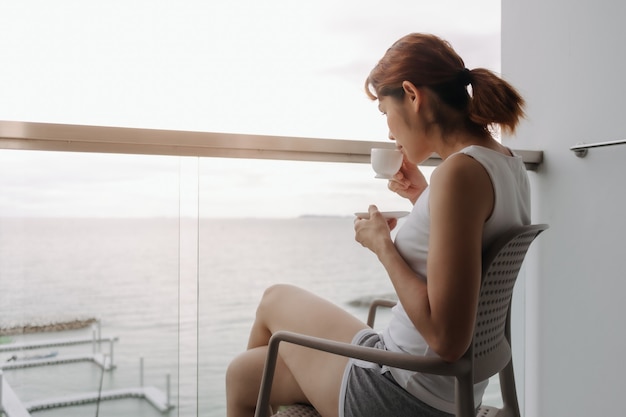 Vrouw drinkt koffie en ontspant op het balkon met uitzicht op zee