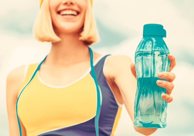 Vrouw drinkwater na het hardlopen Sportmeisje drinkt water uit een fles op een hemelachtergrond Drinken tijdens het sporten