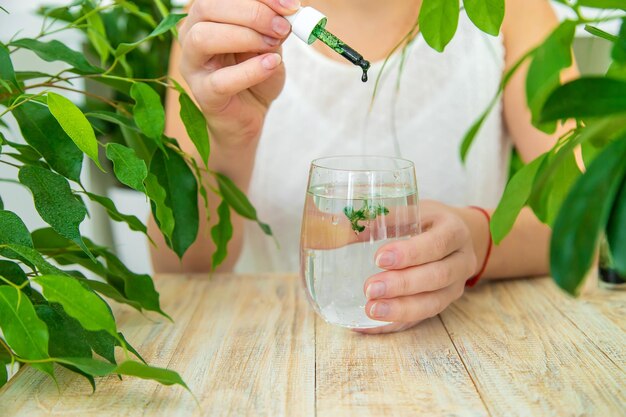 Vrouw druppelt chlorofylsupplement in een glas water Selectieve focus Drinken