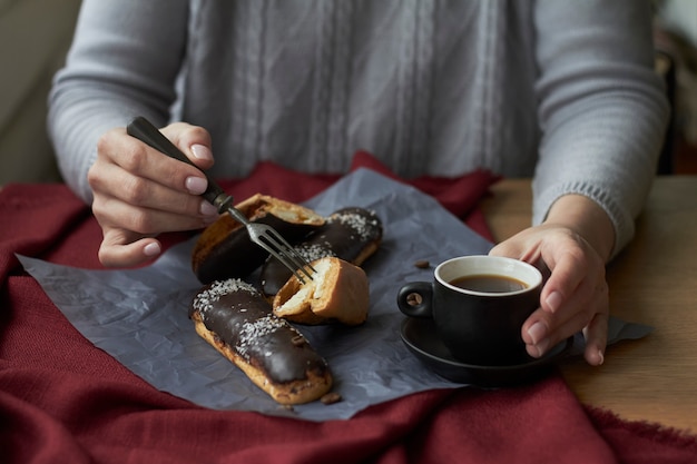 Vrouw eet eclairs gevuld met room, traditionele Franse eclairs met chocolade en kopje espresso.