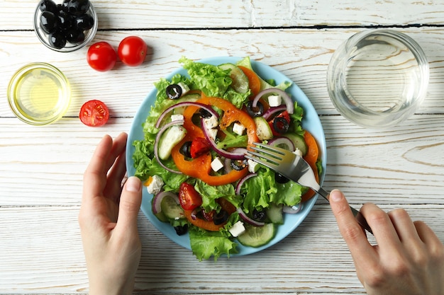 Vrouw eet Griekse salade op witte houten tafel, bovenaanzicht