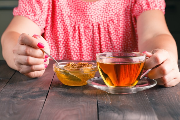 Foto vrouw eet honing en kopje met groene thee op oude houten tafel