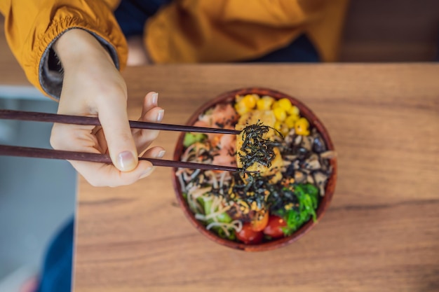 Vrouw eet rauwe biologische poke bowl met rijst en groenten close-up op het tafelblad van bovenaf bekijken