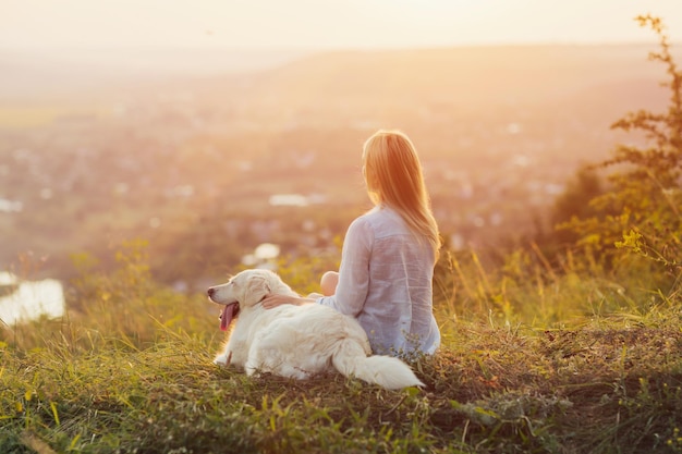 vrouw en de hond zitten op de heuvel en bewonderen het landschap en de zonsondergang