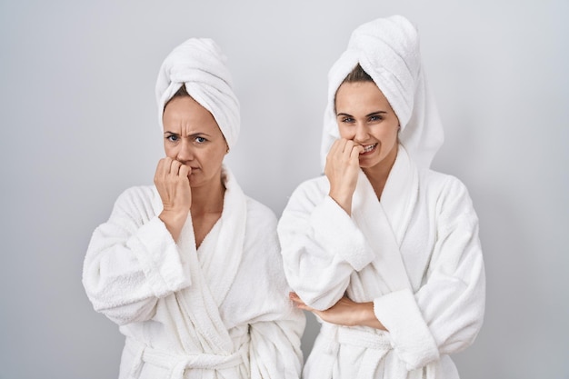 Vrouw en dochter van middelbare leeftijd die witte badjas en handdoek dragen en er gestrest en nerveus uitzien met handen op de mond terwijl ze nagels bijten. angst probleem.