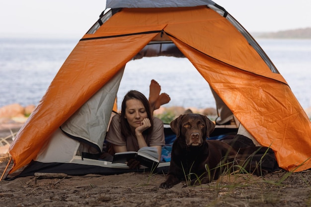 Vrouw en een Labrador retriever hond op een kampeertrip in de natuur een vrouw leest een boek liggend in een tent een huisdier op vakantie met zijn gezin