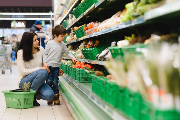 Vrouw en kindjongen tijdens familie die met karretje bij supermarkt winkelen