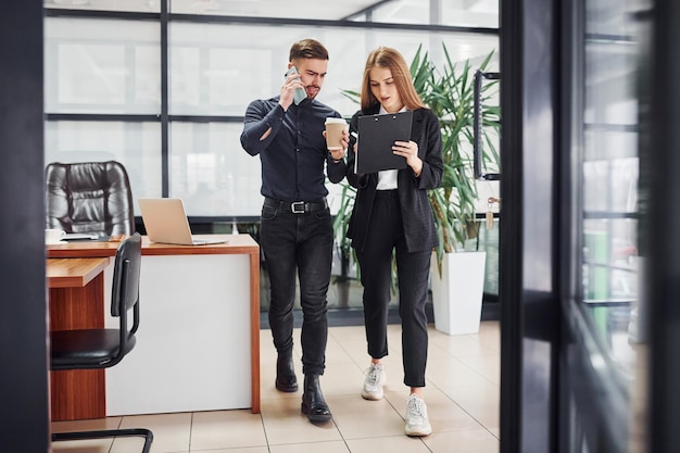 Vrouw en man in formele kleding met documenten die met elkaar praten op kantoor.