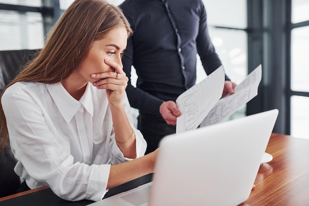 Vrouw en man in formele kleding werken binnenshuis samen op kantoor aan tafel met documenten.