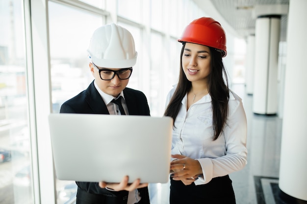 Vrouw en man ondernemer en architect in hemlet op zakelijke bijeenkomst, kijkend naar de laptop op bouwplannen