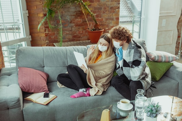 Vrouw en man paar in beschermende maskers en handschoenen thuis geïsoleerd met coronavirusr