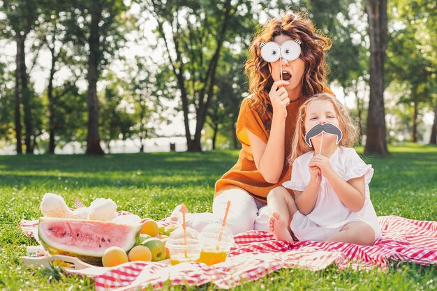 Vrouw en meisje met papieren maskers op de stokken in het park