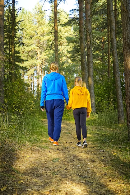 Vrouw en meisje wandelen langs de bosweg in de zonnige dag