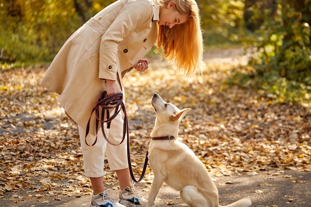 Vrouw en vriendelijke aardige hond in het bos, blonde Kaukasische vrouw in vacht tussen gevallen bladeren op zonnige herfstdag