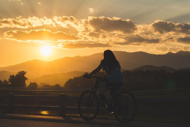 Foto vrouw fietsen op straat tegen de bergen tijdens zonsondergang