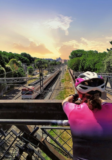 Vrouw fietser vanaf de achterkant en met een helm kijken naar een trein pass van een verhoogde loopbrug.