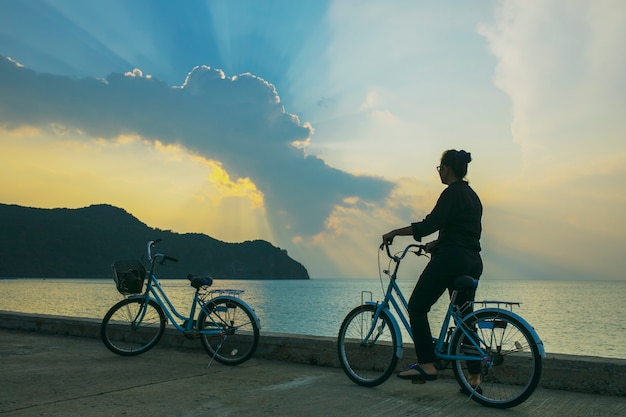 Vrouw fietsten op zee pier tegen dramatische zon lichte hemel