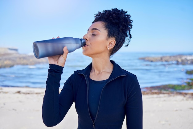 Vrouw fitness en drinkwater over de oceaan voor training, voeding, gezondheid of welzijn buiten Vermoeide hardloper of afrikaanse persoon met vloeibare fles voor energiesporten en cardio