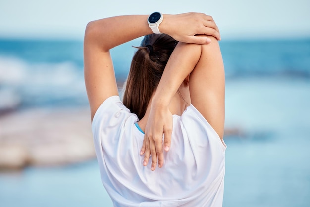 Vrouw fitness en terug op het strand in stretching training of klaar voor training of buitentraining Achteraanzicht van sport vrouwelijke persoon in lichaamsopwarming voorbereiding of gezond wellness door oceaan