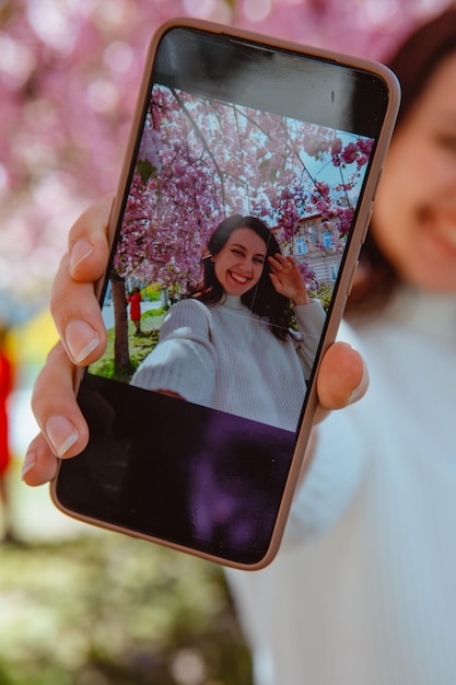 Vrouw fotografeert zichzelf aan de telefoon onder een selfie-foto van een bloeiende sakuraboom