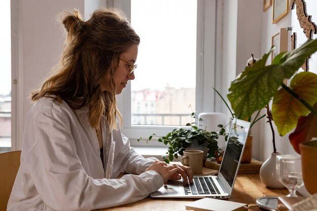 Foto vrouw freelancer / ontwerper werken op de computer vanuit het kantoor aan huis. gezellige werkplek omringd door planten. afstandswerk