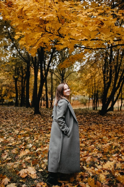 vrouw gaat langs de herfststeeg van het park een meisje in een grijze jas