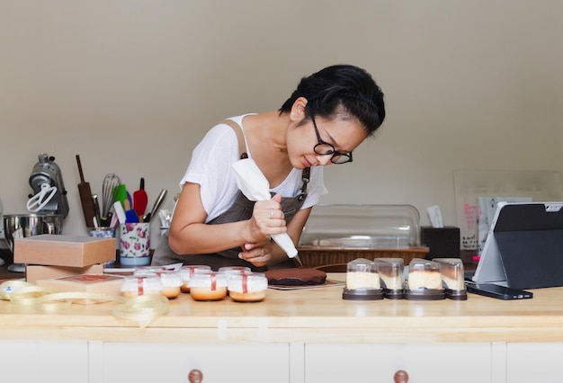 Vrouw gebak met een spuitzak in haar handen knijpt room op een taart in een bakkerij kamer