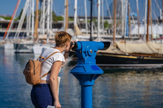 Vrouw gebruikt binoscoop in de haven van Barcelona Blauwe stad verrekijker telescoop voor uitzicht op de stad