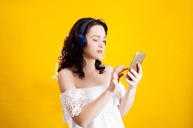 Vrouw gebruikt draadloze hoofdtelefoons en een smartphone binnen over gele muur