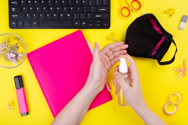 Vrouw gebruikt een antiseptische gel tijdens het werken op de computer, gele achtergrond. pandemische preventie. bovenaanzicht