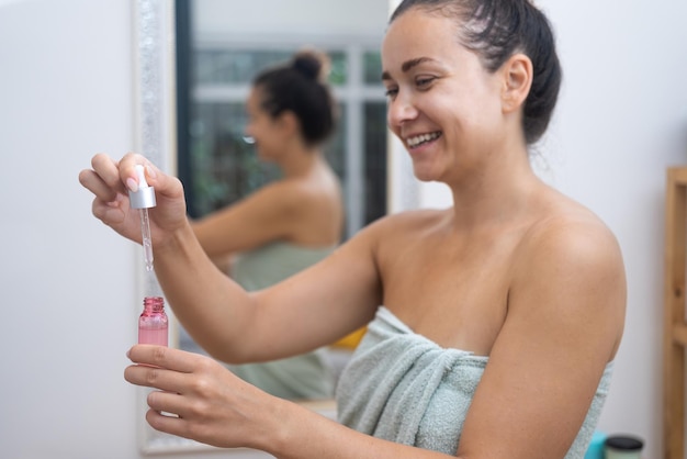 Vrouw gebruikt een serumdruppelaar om hyaluronzuur aan te brengen voor haar anti-aging huidverzorging bij haar spiegel