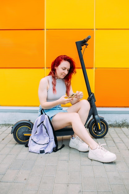 Vrouw gebruikt een smartphone en een elektrische scooter in de zomer in de stad