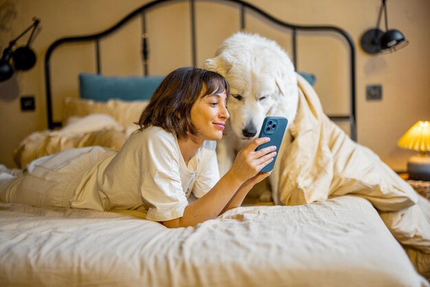 Vrouw gebruikt slimme telefoon terwijl ze met haar schattige schattige hond in bed ligt
