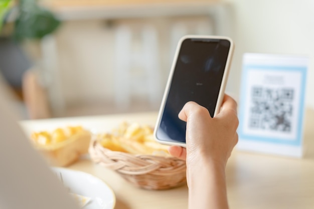 Vrouw gebruikt smartphone om QR-code in café te scannen Het restaurant bouwde een digitaal betalingssysteem zonder contant geld Qr-code betalen E-portemonnee contant geldtechnologie online betalen