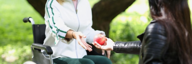Vrouw geeft appel door aan vrouw in rolstoel in parkvriendelijke communicatiewandeling en