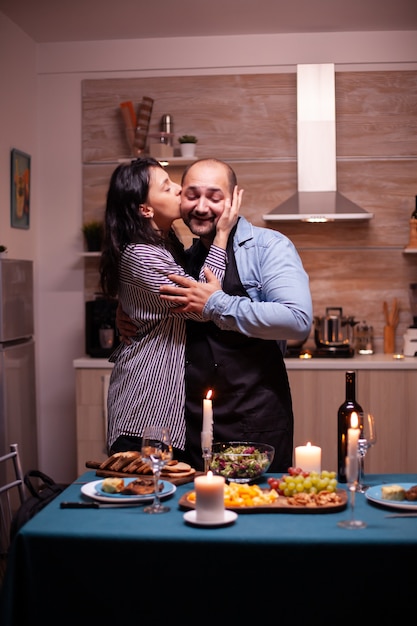 Vrouw geeft echtgenoot genegenheid in de keuken tijdens een romantische date in de avond. Man bereidt feestelijk diner met gezond voedsel, kookt voor zijn vrouw een romantisch diner,