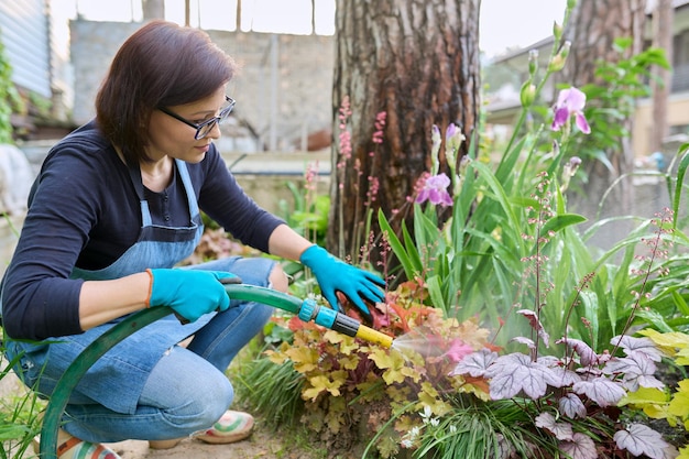 Vrouw geeft planten water in een bloembed in de achtertuin met een tuinslang