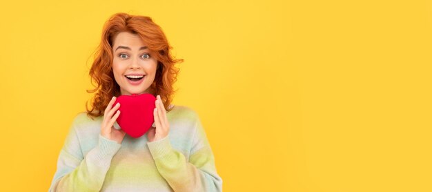 Foto vrouw geïsoleerd gezicht portret banner met kopie ruimte verbaasde roodharige vrouw met rood hart op gele achtergrond