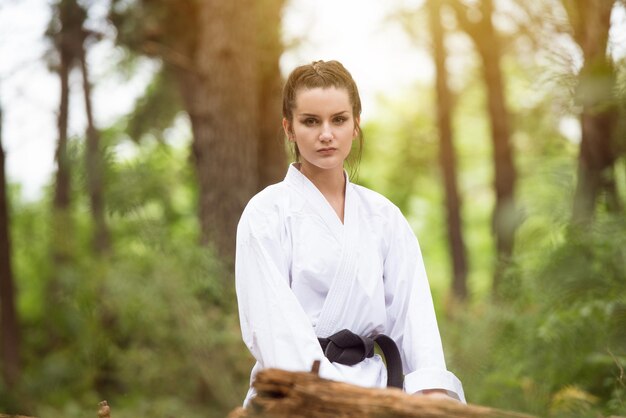 Foto vrouw gekleed in traditionele kimono rust na het beoefenen van haar karatebewegingen in bebost bosgebied