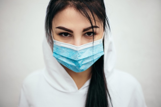 Vrouw gekleed in witte hoodie draagt een blauw wegwerpmasker