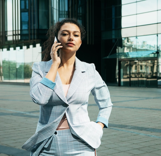 Vrouw gekleed in zakelijke stijl tegen de achtergrond van een zakencentrum houdt een mobiele telefoon vast