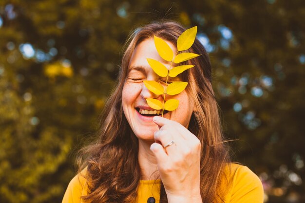 Foto vrouw geniet van de herfst in het park. geel blad op het vrouwelijke gezicht, mooi seizoensportret