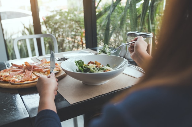 vrouw geniet van het eten Ceasar salade en pizza in het restaurant