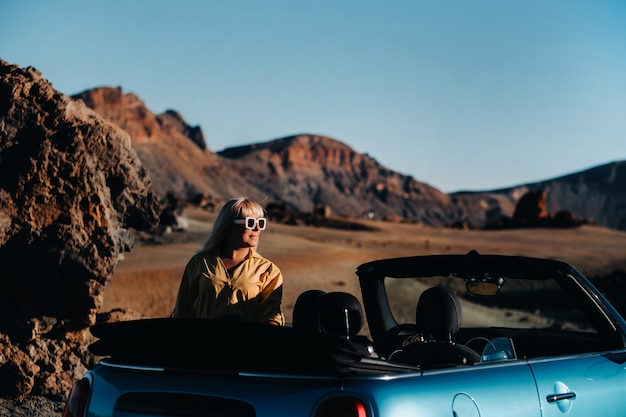 Vrouw genieten van road trip, permanent met kaart in de buurt van converteerbare auto langs de weg in het vulkanische bergbos op het eiland Tenerife, Spanje.