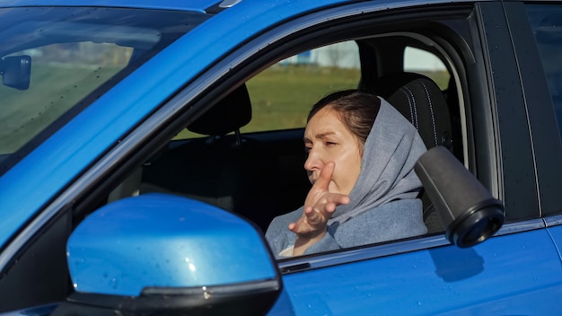 Vrouw gewikkeld in warme sjaal met donkerbruin haar drinkt hete koffie af en gooit plastic beker weg uit autoraam op herfststraat, zijaanzicht